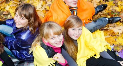 4 nuorta istuu syksyn lehtien peittämällä maalla harteillaan värikkäät viltit