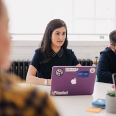 A woman and a man sitting on a desk with laptops