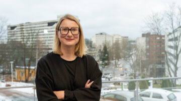 Johanna Kaakinen seisoo kädet ristissä ikkunan edessä, jonka taustalla näkyy Turun kaupunki.