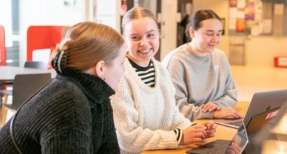 kolme henkilöä istuu pöydän ääressä tietokoneet edessään.