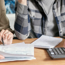 Kaksi tunnistamatonta henkilöä pöydän ääressä tutkimassa laskuja.