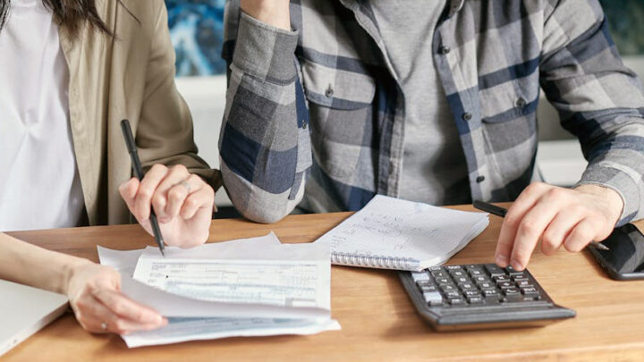 Kaksi tunnistamatonta henkilöä pöydän ääressä tutkimassa laskuja.