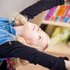 Nuori venyttelee kirjahyllyn edessä.