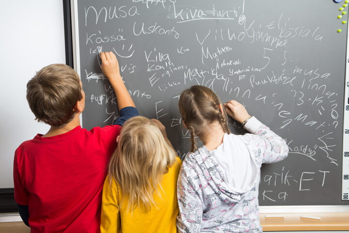 Koululaiset kirjoittavat liitutaululle.