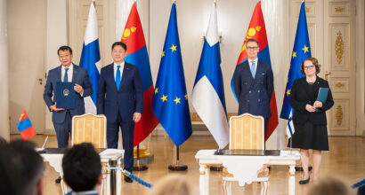neljä ihmistä seisoo Suomen ja Mongolian lippujen edessä hyvin virallisesti.