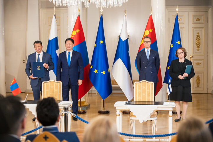 neljä ihmistä seisoo Suomen ja Mongolian lippujen edessä hyvin virallisesti.